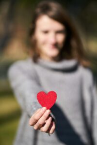 A woman presenting a red heart symbol, showcasing love and compassion.